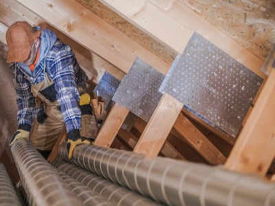 An HVAC technician installing duct work in an attic.
